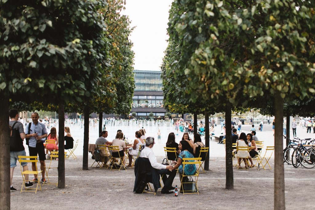 People sitting in outdoor cafés in a square with a fountain
